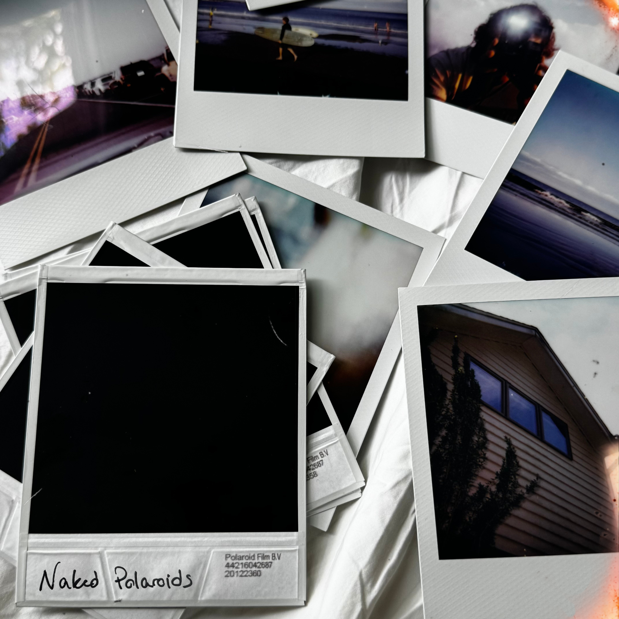 Naked Polaroids cover art: a scattered pile of polaroid photographs on a bed, one blank frame hand-labeled "Naked Polaroids"
